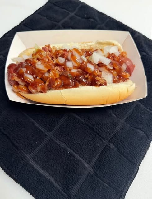 A weiner covered in chili and diced onions in a paper tray