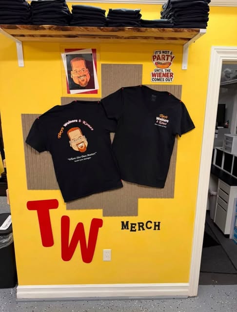 Two black Tiny's t-shirts pinned to the yellow merch wall