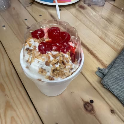 Sundae in a cup topped with cherries on a wooden table